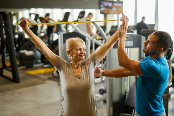 Mann Anfang 60 macht Übungen mt einem gelben Fitnessband in seinem Wohnzimmer