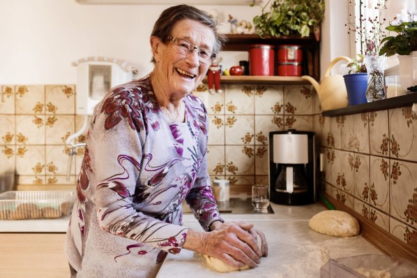 Eine Seniorin knetet einen Teig in ihrer Küche und freut sich.