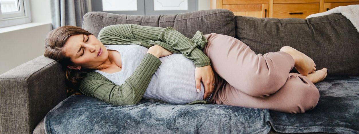 Schwangere Frau liegt mit Schmerzen im Bauch auf der Couch,