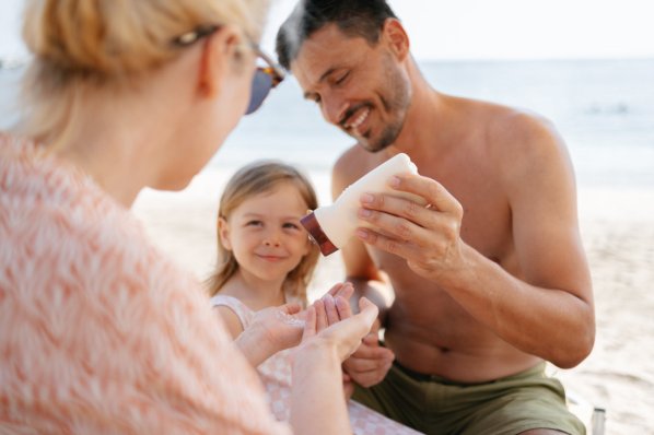 Familienvater drückt Sonnencreme aus der Flasche auf die hand seiner Frau