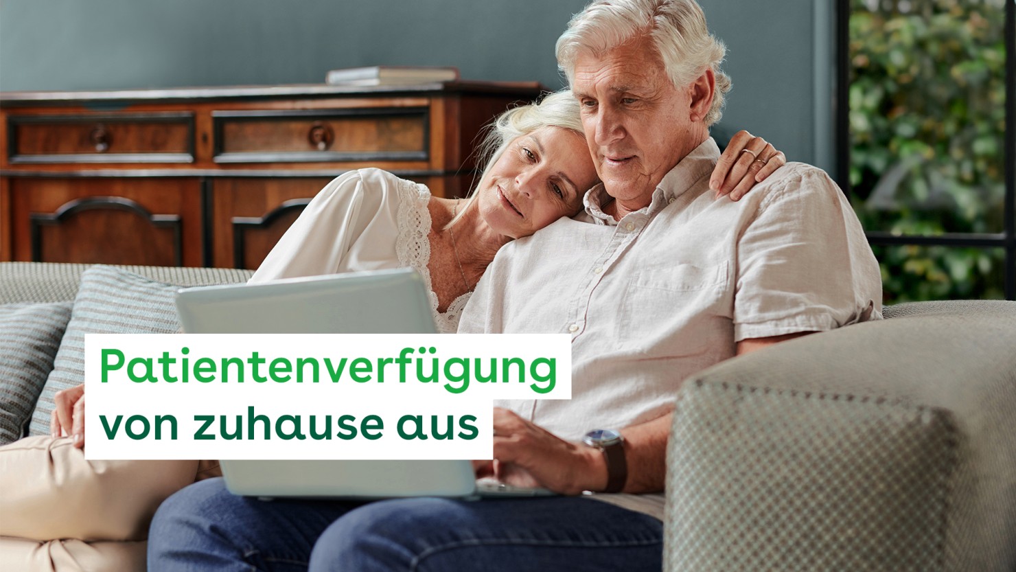 Ein senior Paar sitzt zu Hause auf dem Sofa. Er hat einen Laptop auf den Beinen liegen. Beide schauen auf den Bildschirm.