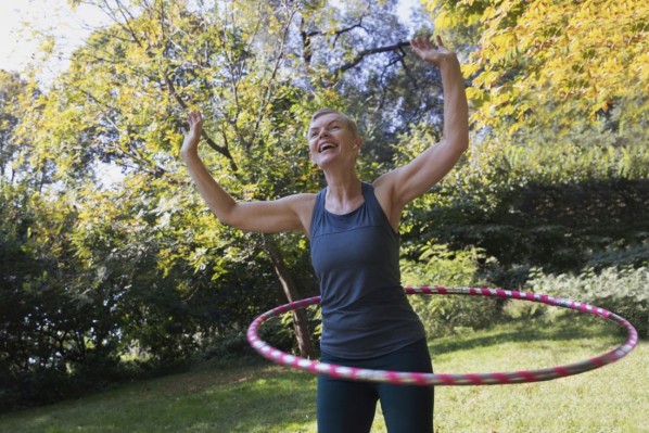 Zwei etwa 7 jährige Mädchen spielen gemeinsam in der Natur mit einem Hula Hoop-Reifen.