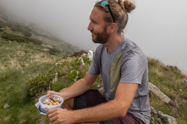 Ein Mann macht eine Wanderpause und isst zu Stärkung Nüsse und Saaten.
