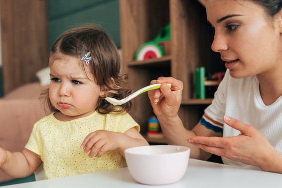 Ein wählerisches Kleinkind wird von seiner Mama gefüttert.