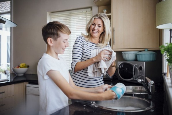 Eine Mutter wäscht gemeinsam mit ihrem etwa 13-jährigen Sohn das Geschirr in der Küche ab.