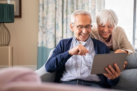 Ein Seniorenpaar schaut gemeinsam lächeln auf ein Tablet.