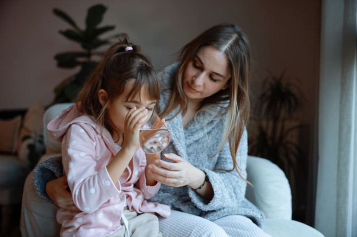 Eine Mutter reicht ihrer Tochter mit Norovirus Flüssigkeit