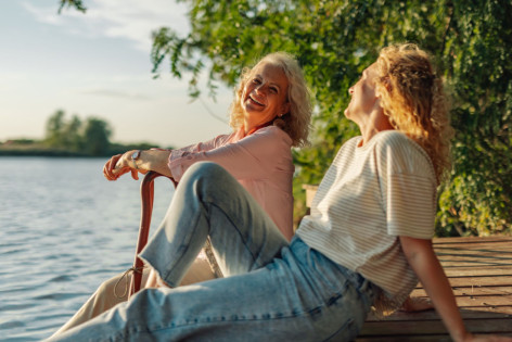 Zwei Frauen sitzen auf einem Steg am See und freuen sich, dass sie durch Hypnose mit dem Rauchen aufgehört haben.