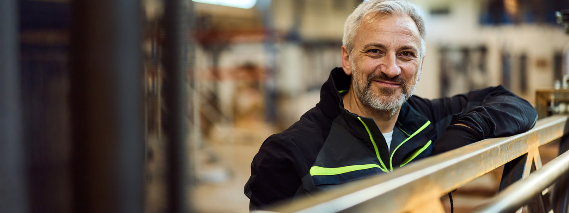 Lächelnder älterer Mann in Arbeitskleidung in Industriehalle