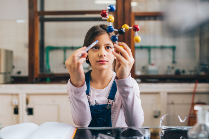 10-jähriges Mädchen mit Molekülmodell im Chemie-Klassenraum