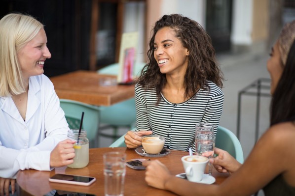 Eine drei Frauen sitzen in einem Cafe und unterhalten sich. Sie lachen ausgiebig.