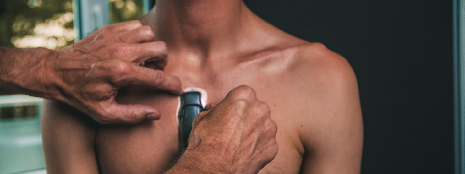 Ein männlicher Oberkörper wird ein Langzeit-EKG-Rekorder auf den Oberkörper geklebt.
