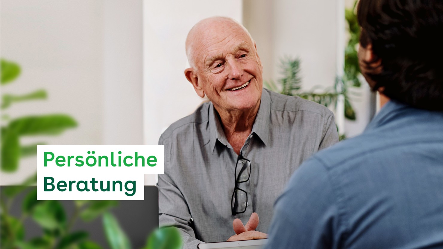 Ein etwa 70jähriger Mann sitzt an einem Tisch und unterhält sich mit einer weiteren Person.
