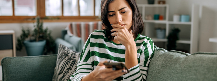 Eine etwa 40-jährige Frau prüft skeptisch ihr E-Mails auf ihrem Smartphone.