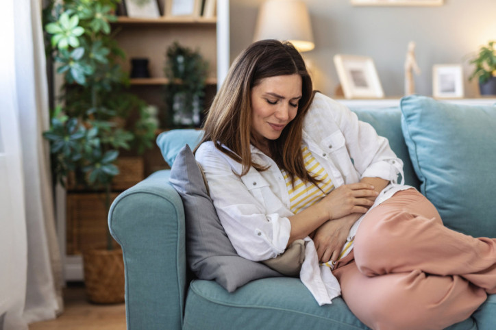 Eine Frau hat ziehende Schmerzen im Unterbrauch beim Liegen