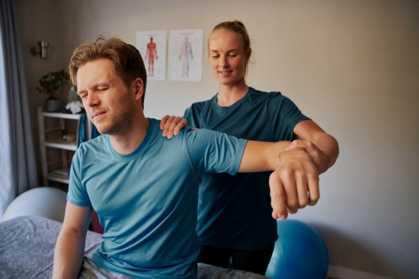 Junger Mann erhält Physiotherapie. Er schaut mit scherzverzerrtem Blick.