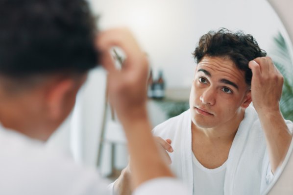 Junger Mann Ende 20 zupft an seinen braunen Locken