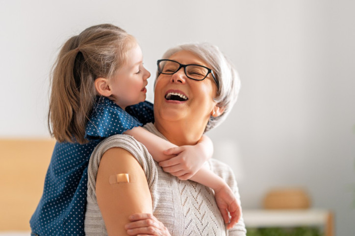 Enkelin umarmt ihre Oma von hinten. oma hat ein kleines Pflaster am Oberarm