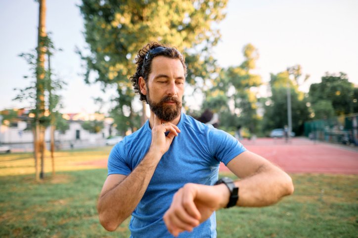 Ein Sportler fühlt seinen Puls am Hals und schaut auf seine Smartwatch.