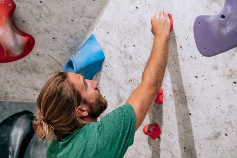 Ein junger Mann hängt an einer Kletterwand in einer Boulder-Halle.