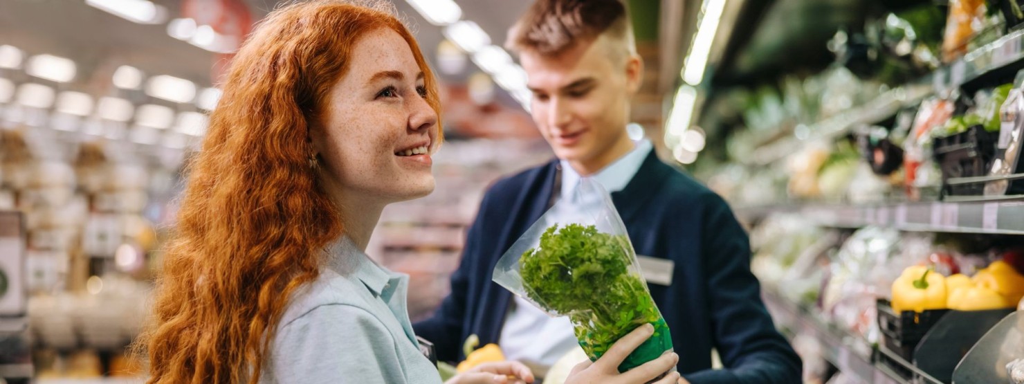 Zwei junge Aushilfen räumen gemeinsam das Gemüseregal in einem Supermarkt ein.