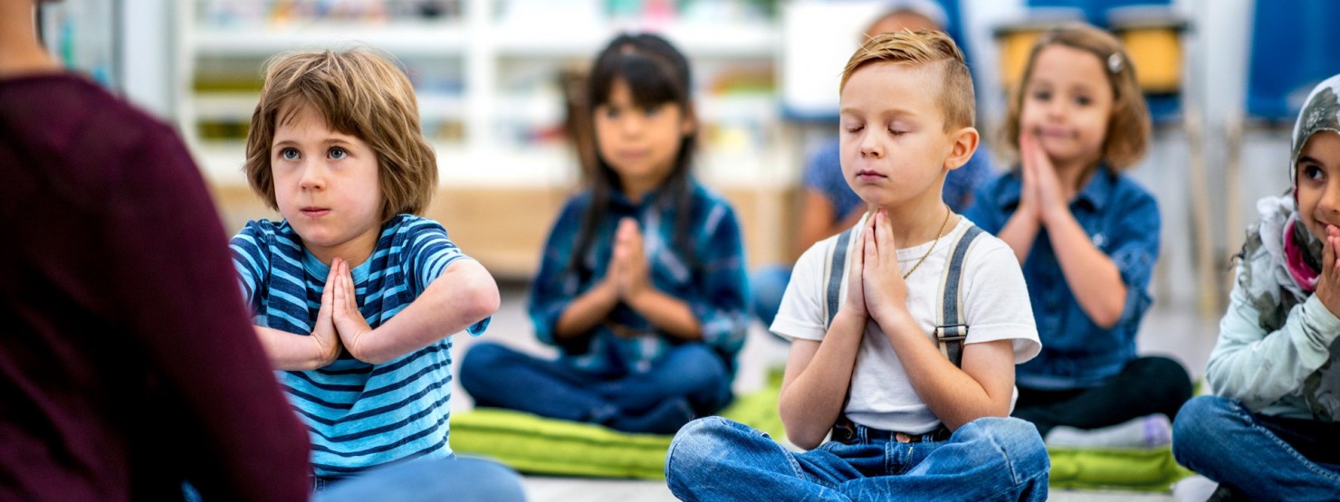 Kinder sitzen im Schneidersitz auf Matten und meditieren.