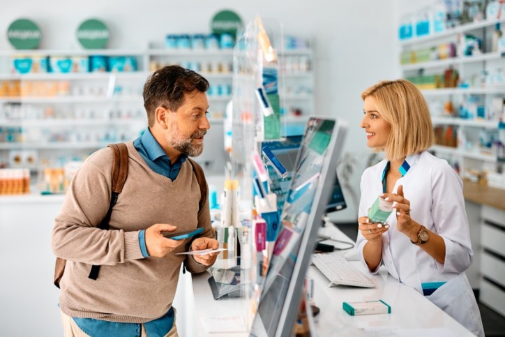 Happy man advising with his pharmacist while taking prescription medicine in a pharmacy.