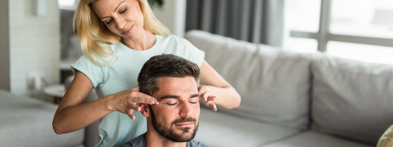 Ein Mann erhält von seiner Partnerin eine Akupressurmassage am Kopf.