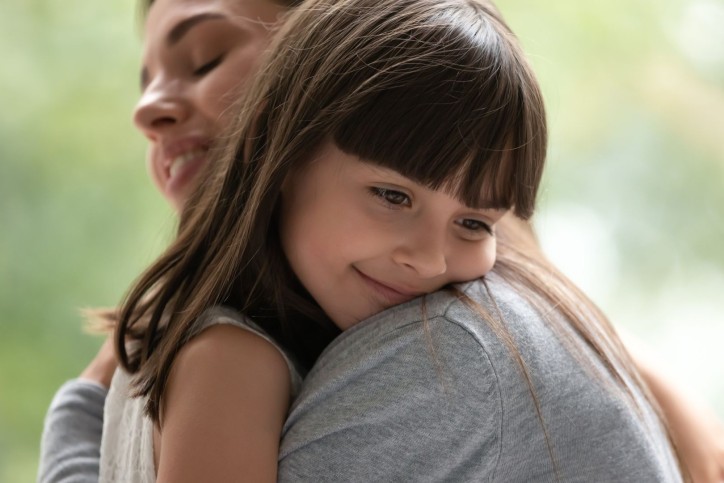 Ein etwa 5 jähriges Mädchen liegt in dem Armen ihre Mutter. Sie lächelt.