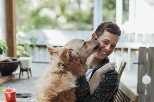 Ein etwa 30 jähriger Mann spielt ausgelassen mit seinem Hund.