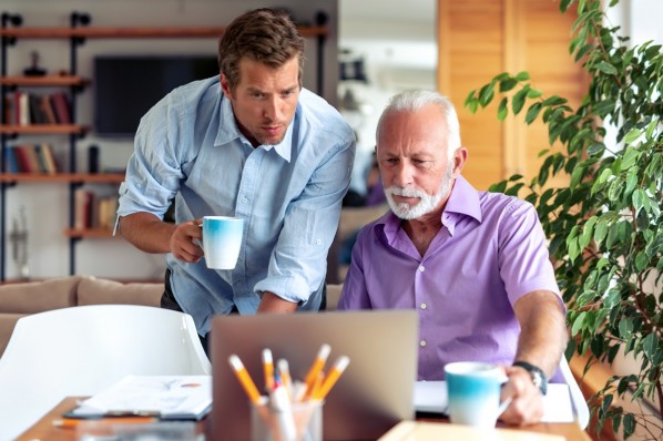Ein 40-jähriger Mann und sein 70-jähriger Vater schauen zusammen auf einen Laptop.