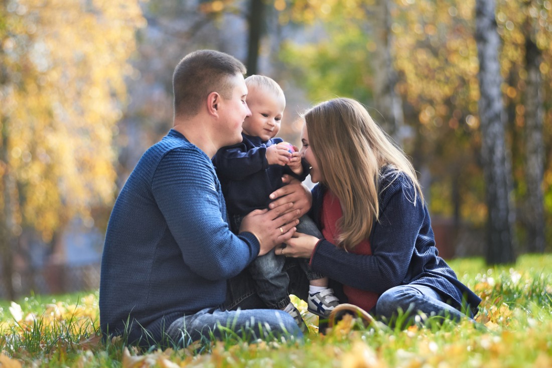 Eine dreiköpfige Familie sitzt auf einer Wiese und spielt und lacht gemeinsam.