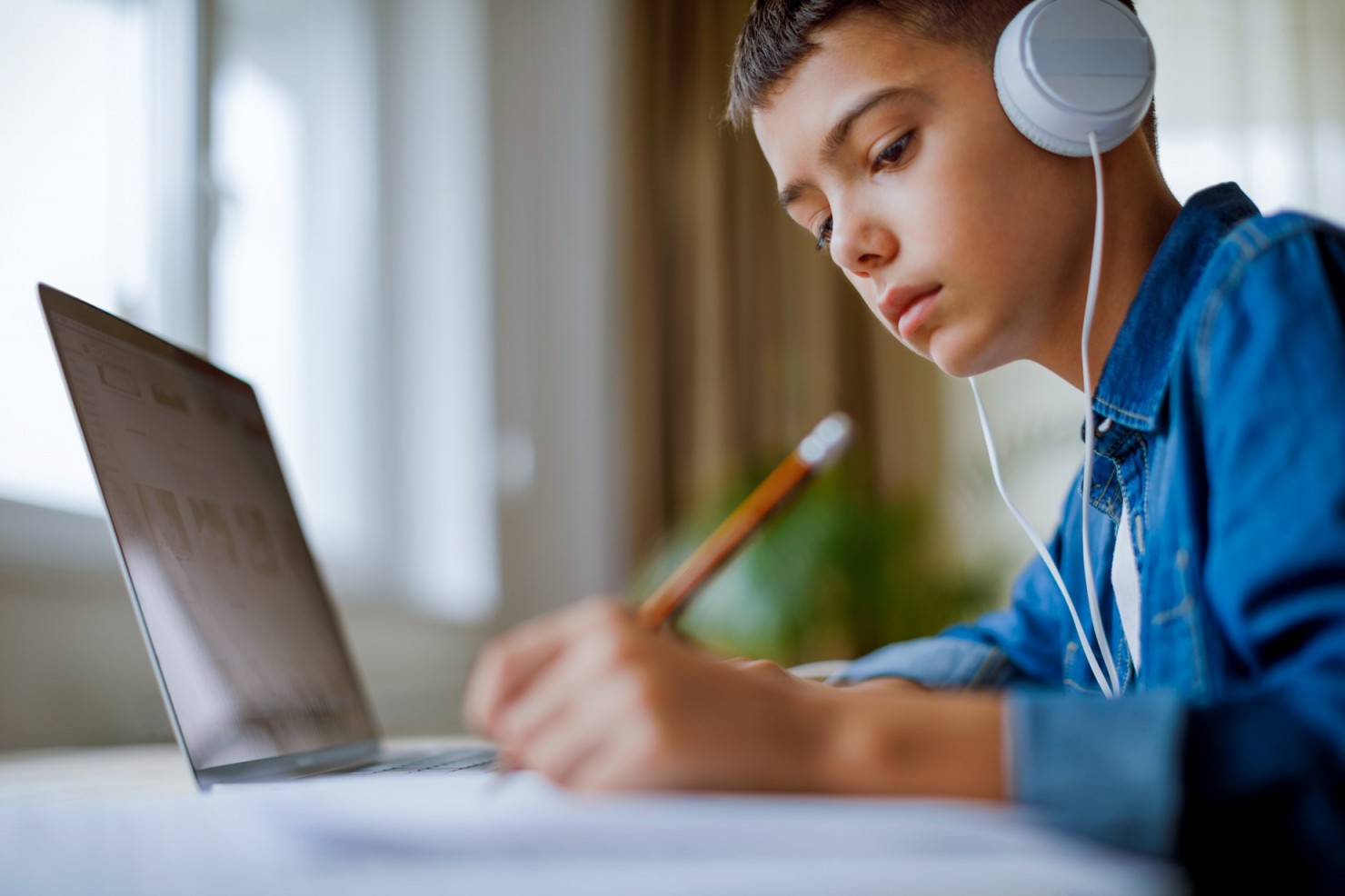 Ein circa 12jähriger Junge hört Musik während er seine Hausaufgabe macht. 