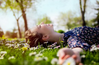 Lächelnde junge Frau liegt auf einer Wiese mit Gänseblümchen