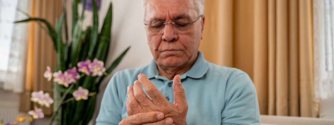 Ein Senior überprüft seine linke Hand auf Anzeichen von Rheuma.