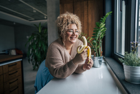 Frau lehnt an der Küchentheke und isst eine Banane