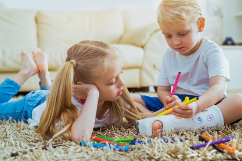 Zwei Kinder sitzen auf dem Boden und bemalen einen Fußgips.