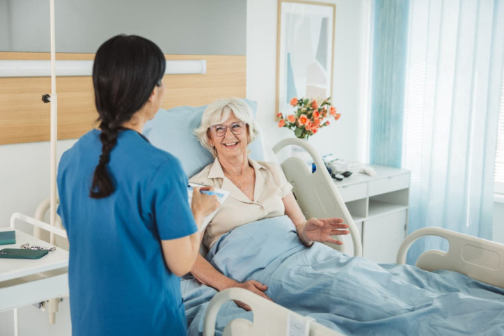 Krankenschwester begrüßt freudige ältere Patientin, die im Krankenbett liegt