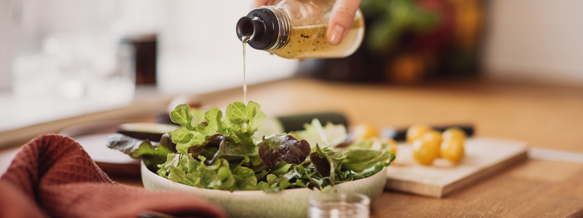 Eine Hand gießt Essig über einen Salat.
